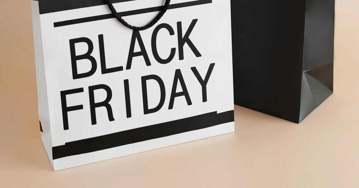 A white paper shopping bag printed with Black Friday next to a plain black shopping bag