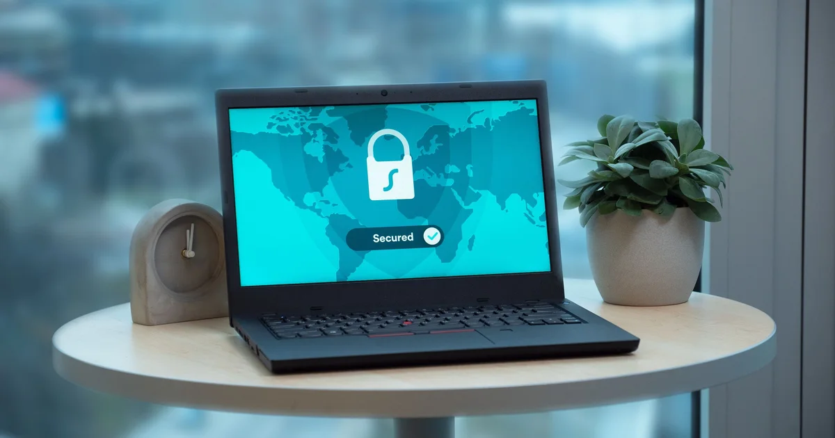 A laptop on a small round table showing a padlock and the word Secured, next to a plant and a clock