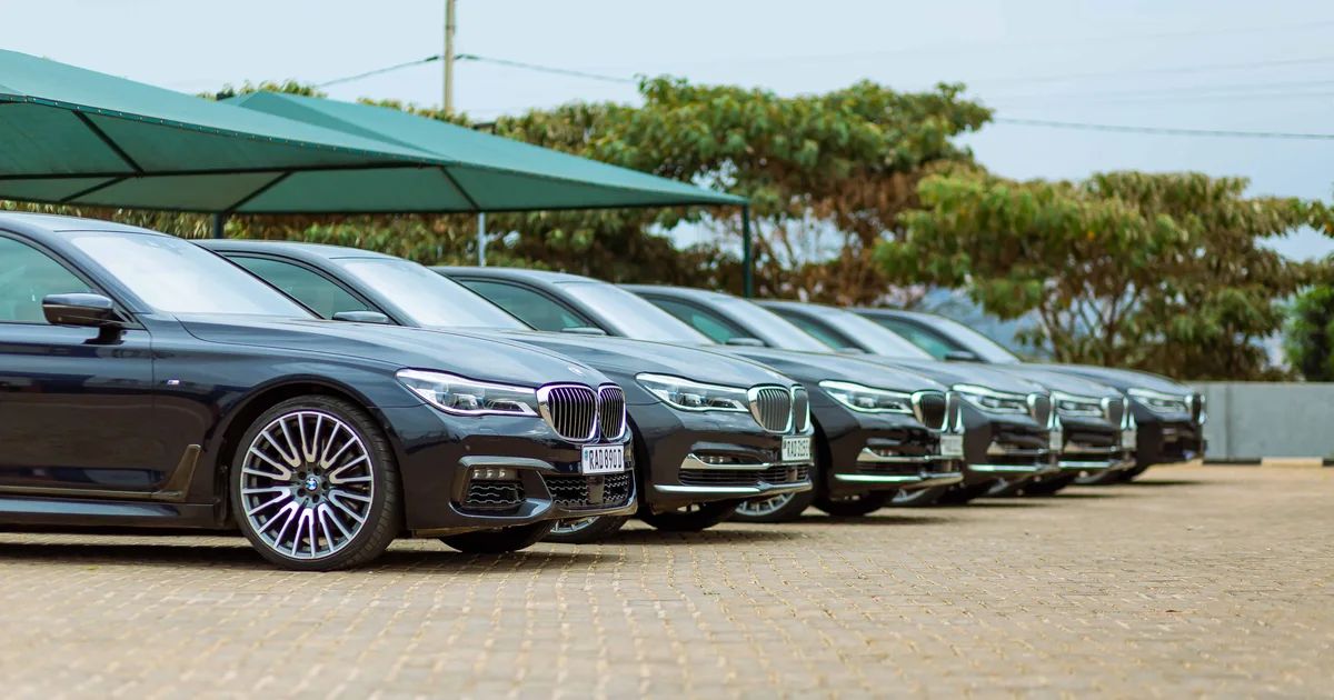 A row of dark saloon cars parked under shade canopies at an outdoor car dealership