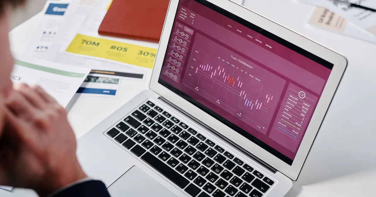An open laptop showing a purple line chart on an analytics dashboard, with printed reports on the desk