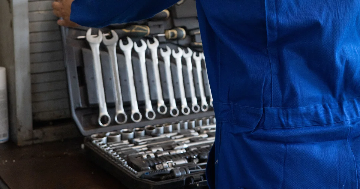 A technician in blue overalls beside an open toolbox of spanners and sockets