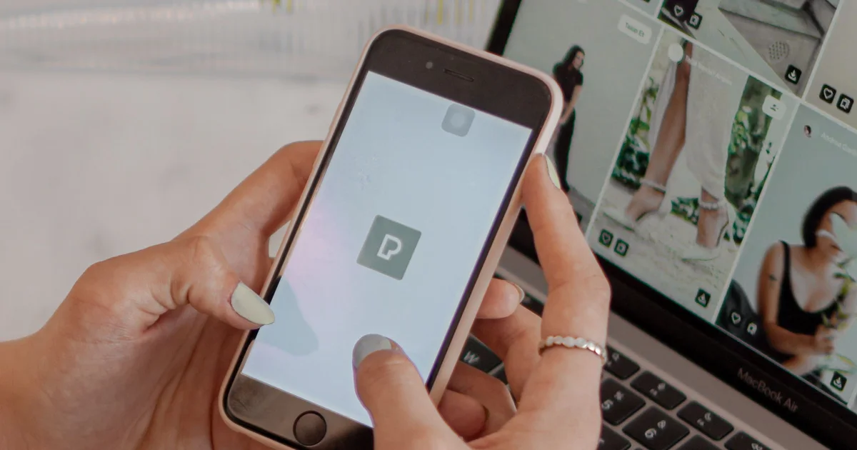 Hands holding a smartphone in front of a laptop showing an online shop, the moment after someone taps an ad