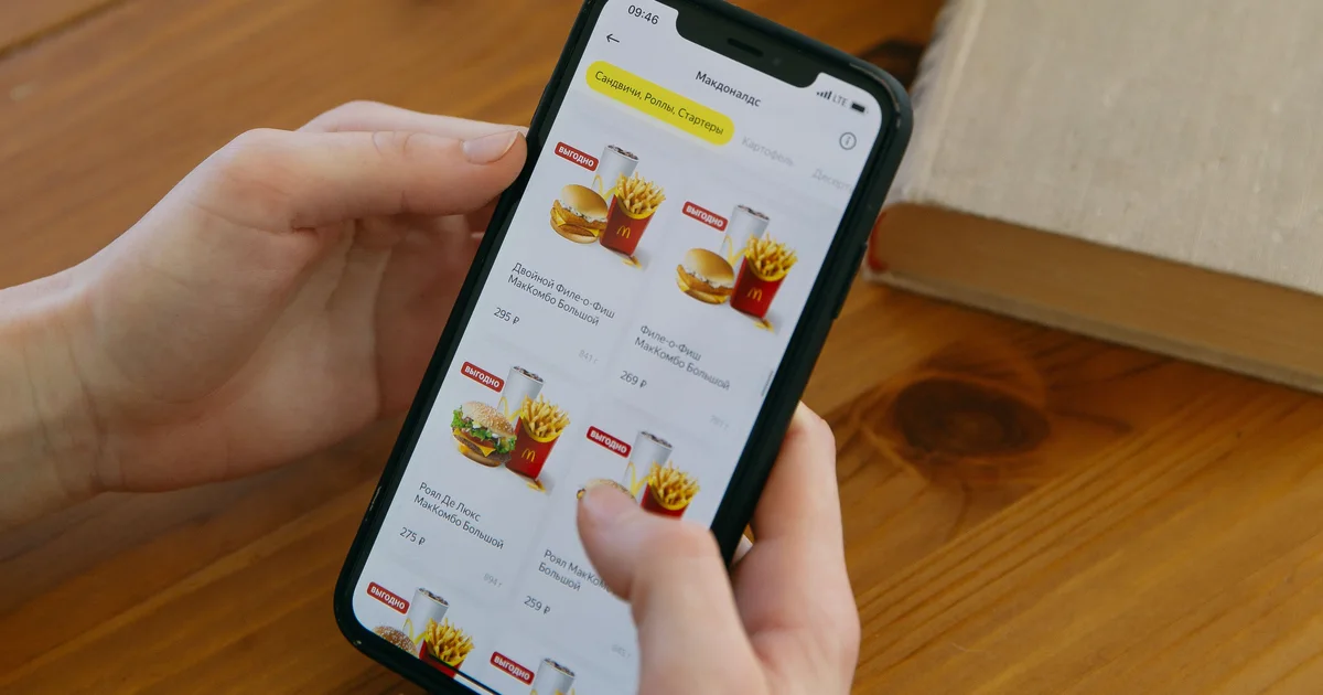 Hands holding a smartphone showing a food ordering app, next to a potted plant on a wooden table