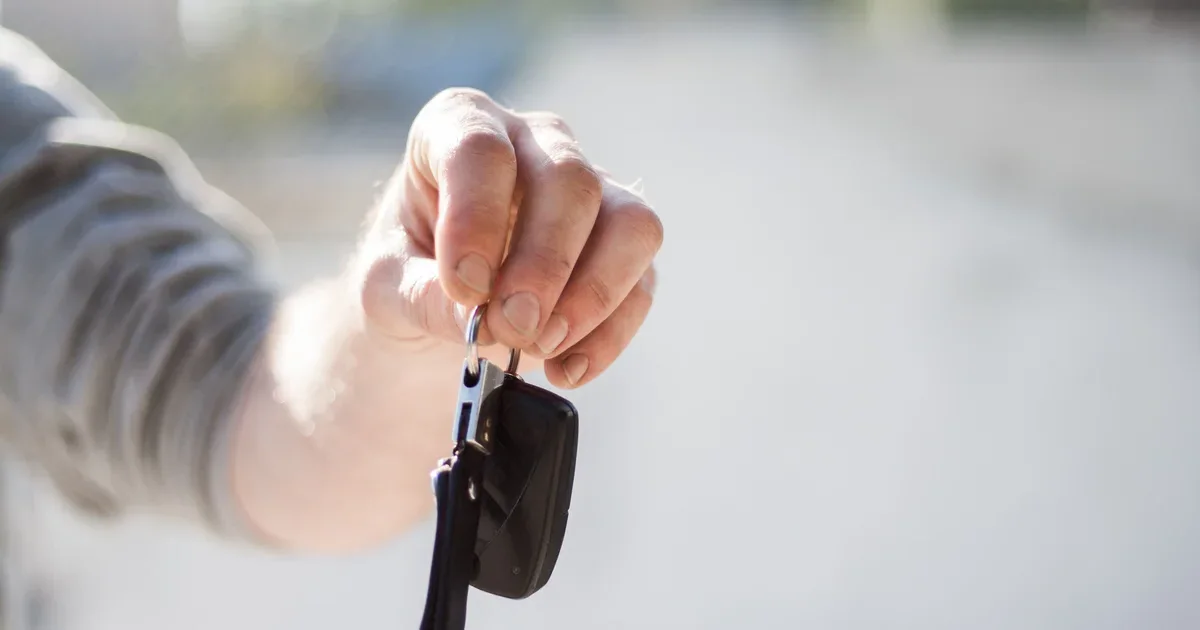 A hand holding up a car key against a blurred street background